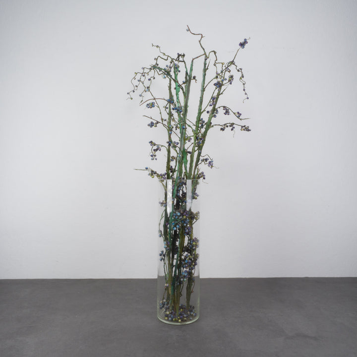 Large glass vase with beautiful branches of fake eucalyptus fruits in blue and green